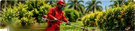 Worker in red overalls trimming a hedge at a commercial property